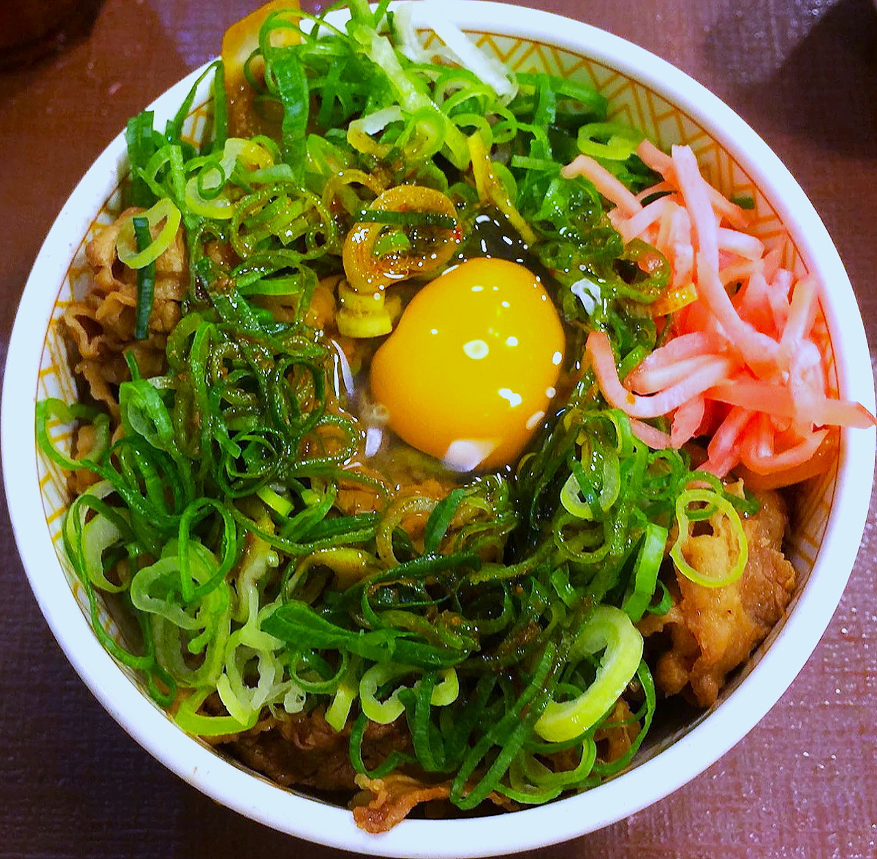 Overhead photo of gyudon beef bowl with egg yolk, green onions, and pickled ginger