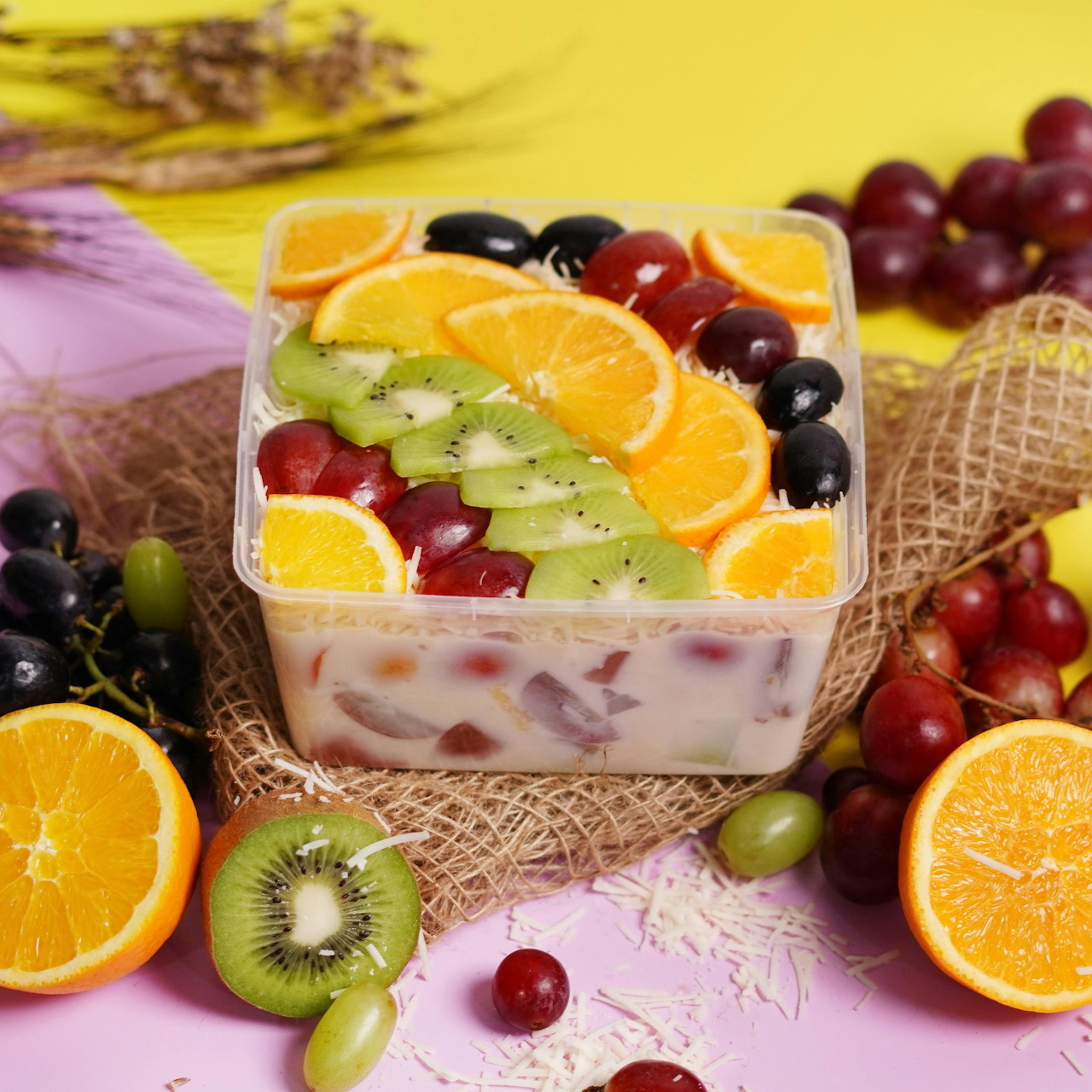 Square fruit cake topped with kiwi, orange slices, grapes, and berries on a colorful table