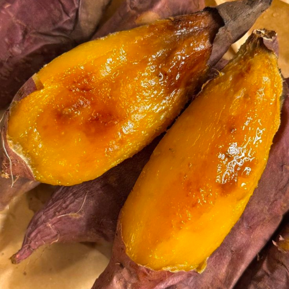 Two halves of a baked sweet potato showing caramelized orange flesh on purple skin