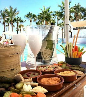Champagne bottle, pink cocktails, and appetizer platter with dips and vegetables at a tropical pool
