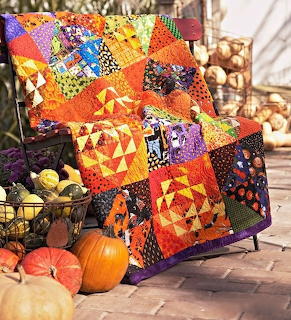 Handmade Halloween patchwork quilt with orange and black patterns draped over chair with pumpkins