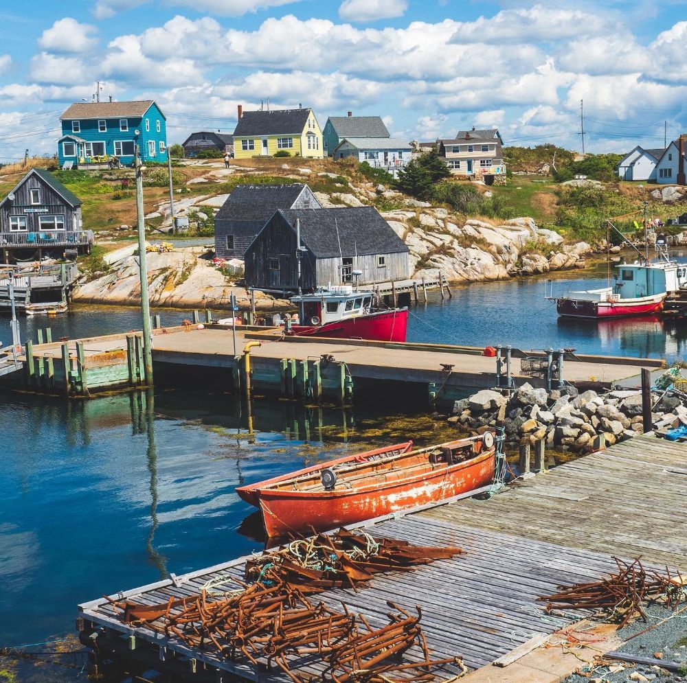 Fishing boats docked at a small coastal harbor with colorful houses on a rocky hillside
