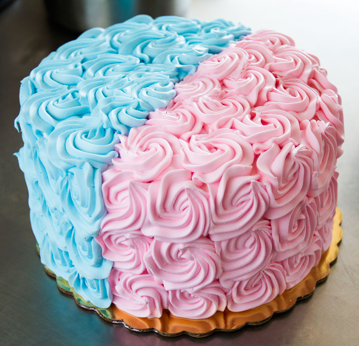 Round cake decorated with pink buttercream rosettes on one half and blue rosettes on the other half