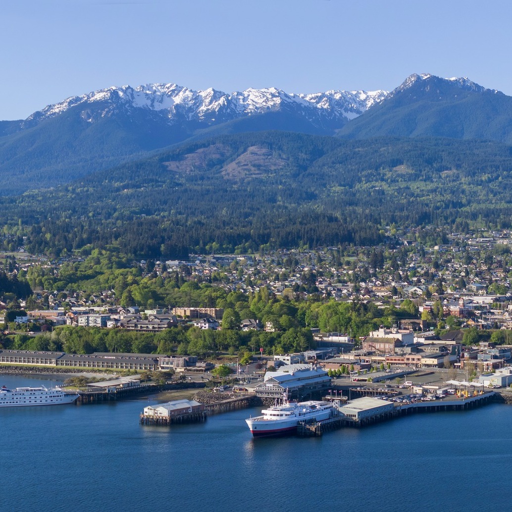 Waterfront city with ferries, piers, and snow-capped mountains in the background