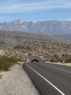 Road leading to a tunnel through rocky desert landscape with layered mountain cliffs in Big Bend National Park