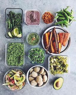 Overhead flat lay of glass meal prep containers with vegetables, roasted carrots, chickpeas, kale, and avocado
