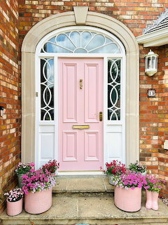 Pink front door with arched transom window, white sidelights, and pink flower pots on a brick house