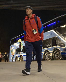 Soccer player in red hoodie walking near team bus at night