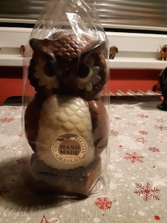 Hand-made chocolate owl figurine in brown and white wrapped in clear plastic on a red tablecloth