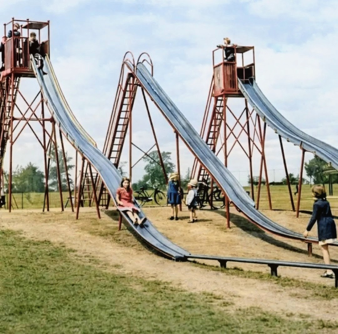 Vintage colorized photo of children on tall playground slides in a grassy park