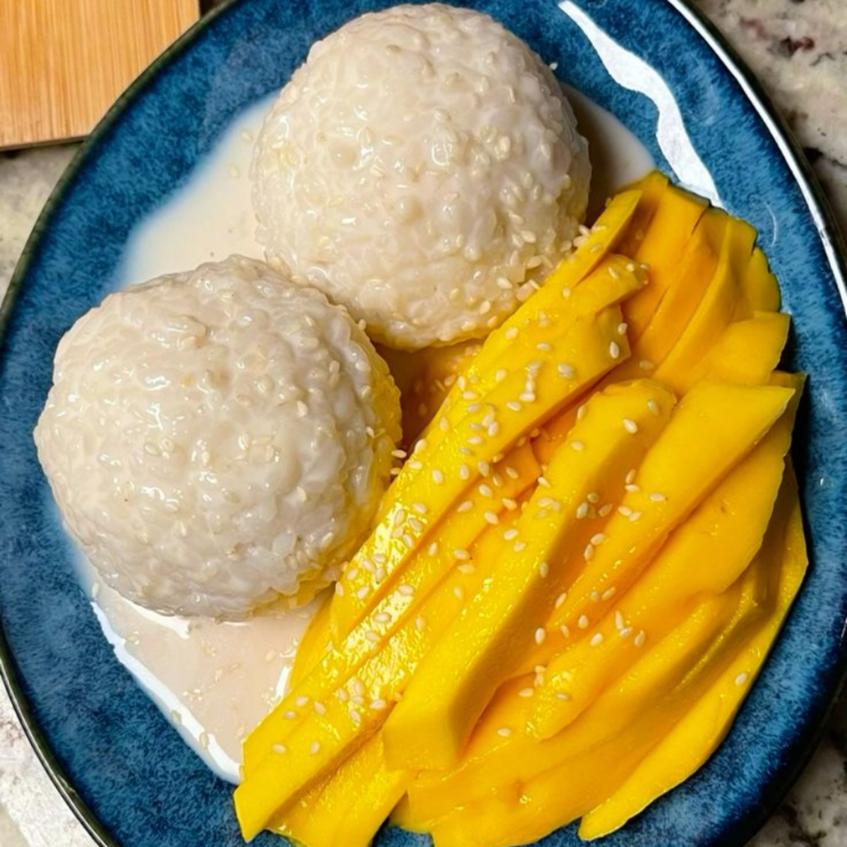 Mango sticky rice dessert with sliced yellow mango and coconut cream in blue bowl