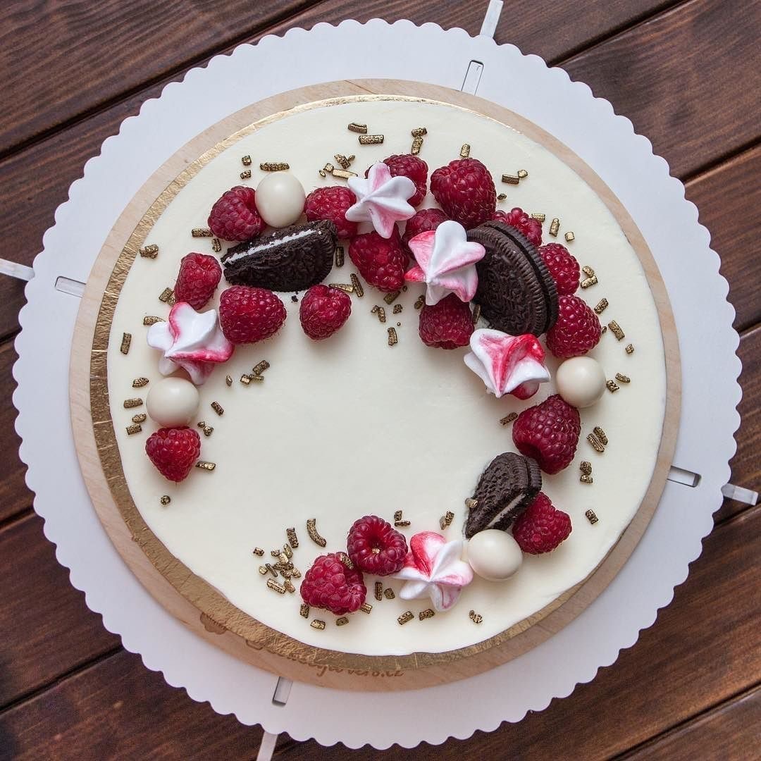 Round cake topped with raspberries, strawberries, chocolate cookies, meringues, and pistachios on white platter