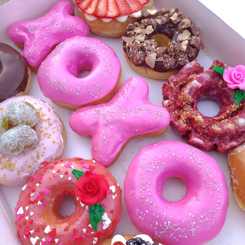 Assorted pink frosted and decorated donuts in a box with heart sprinkles and Valentine-themed toppings