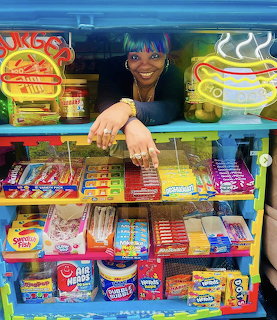 Smiling vendor at vibrant candy stand with colorful sweets and gum displays