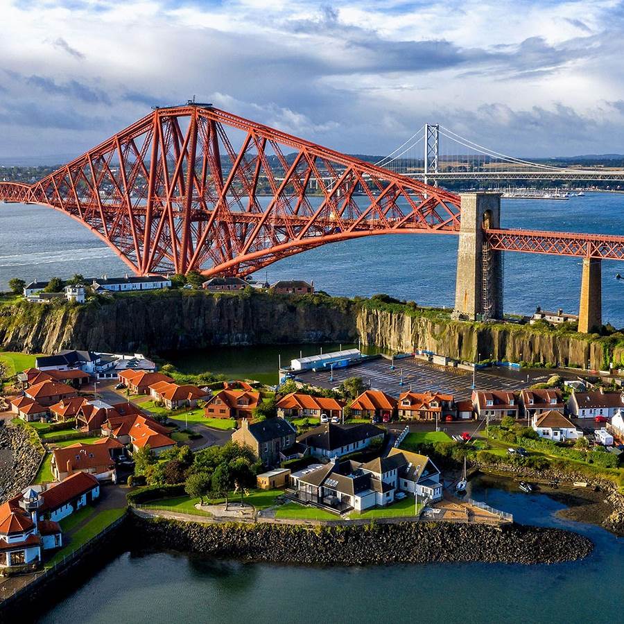 Aerial view of red Forth Bridge over water with village below and cloudy sky