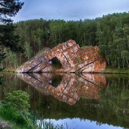Weathered rock formation reflected in still water with birch forest background