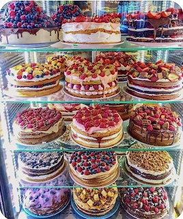 Glass bakery display case with shelves of decorated layer cakes topped with berries and fresh fruit