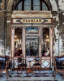 Ornate facade of Caffè Florian in Venice with gilded sign, mirrors, and antique chairs on a tiled floor