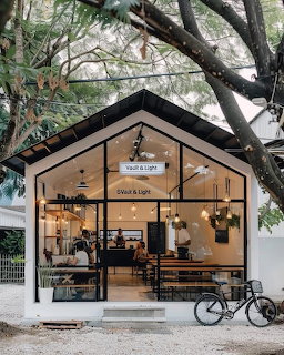 Small cafe with glass facade and warm lighting surrounded by green trees with a bicycle parked outside