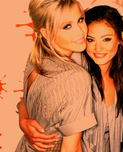 Two smiling young women, one blonde and one brunette, posing closely together in matching gray outfits.