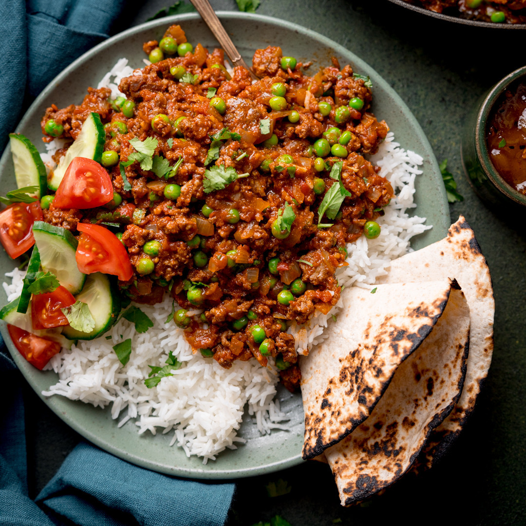 Plate of spiced minced meat with peas, white rice, salad, and charred flatbread