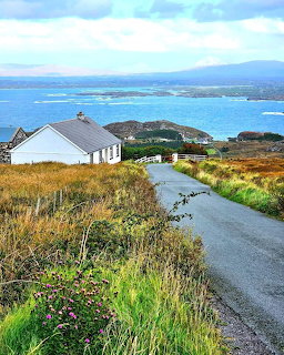 White cottage beside rural road with ocean and hills in background