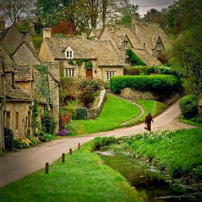 Traditional stone cottages with thatched roofs in a verdant English village setting with a stream and path