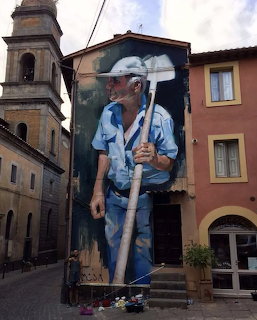 Large street art mural of an elderly man holding a hoe painted on building wall in Italian town