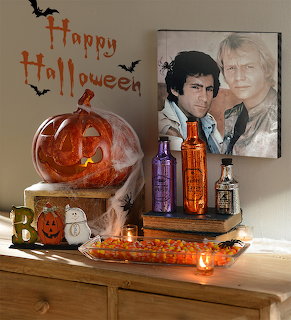 Halloween decorations on a wooden dresser with a jack-o'-lantern, cobwebs, candles, and a framed portrait