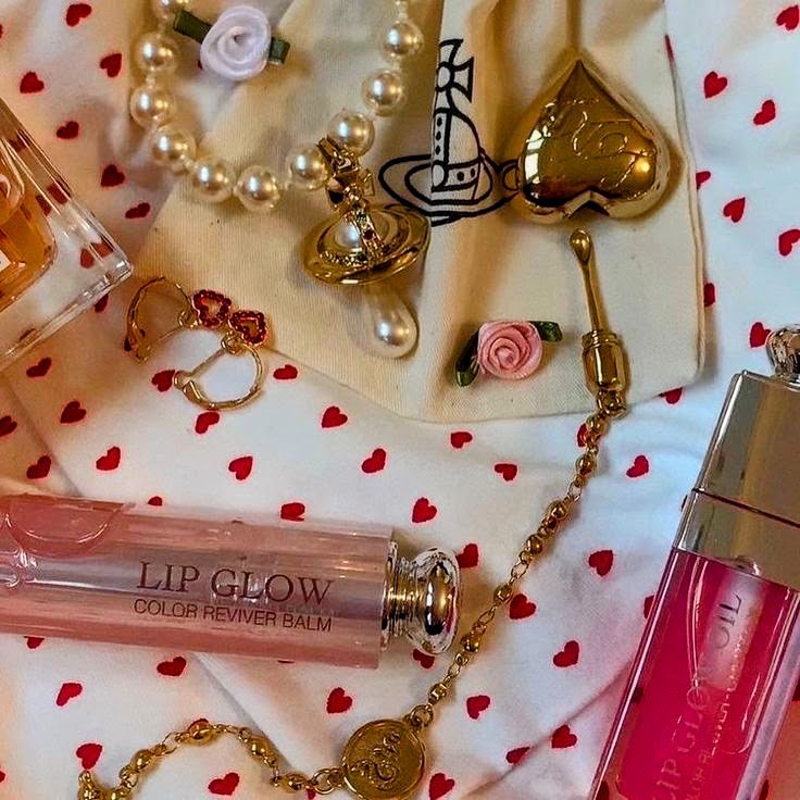 Lip gloss, rings, pearls, and gold heart accessories on white fabric with red hearts