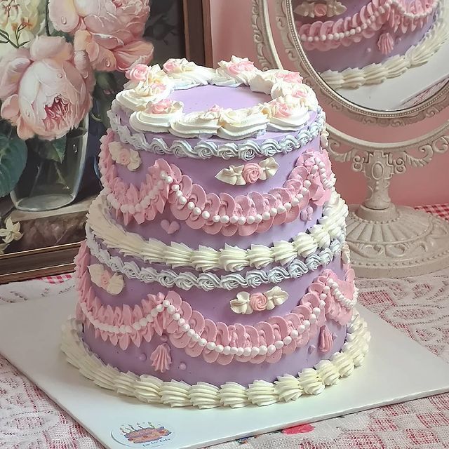 Two-tier purple cake with pink ruffles and white piped decorations on vintage lace