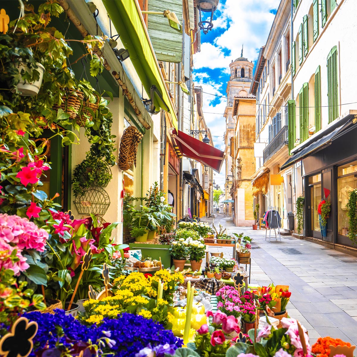 Colorful flower-filled narrow street in Arles France with old buildings and a church tower