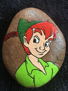 Painted rock featuring a colorful cartoon boy on a dark fabric background