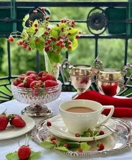 Vintage tea set with strawberries and flowers on windowsill overlooking garden