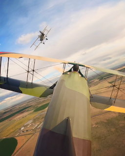 View from a vintage biplane with another biplane flying above over farmland