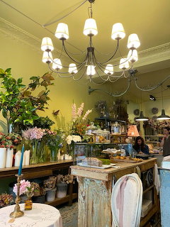 Interior of a flower cafe with chandelier, floral arrangements, vintage decor, and a person behind the counter