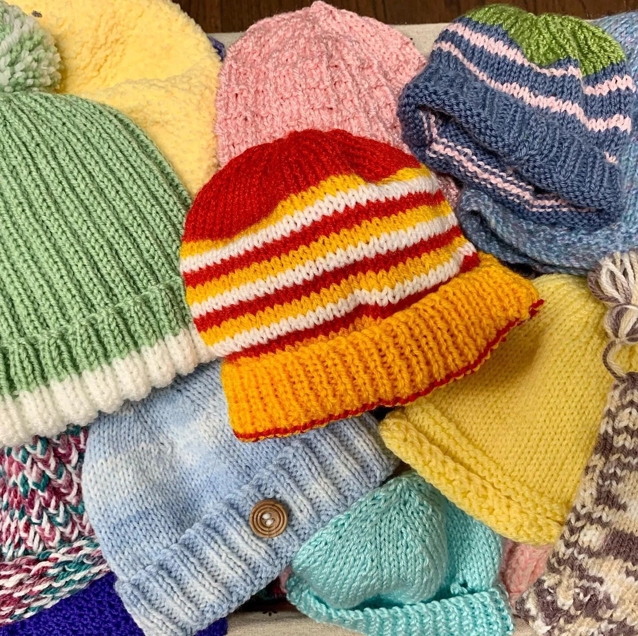 Pile of colorful hand-knitted winter hats in yellow, pink, blue, orange, green, and striped patterns