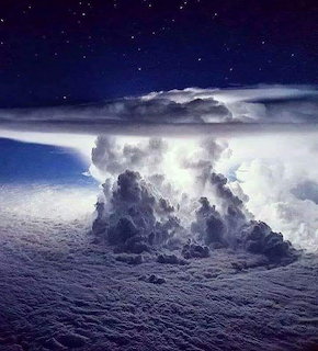 Towering storm cloud lit from within by lightning viewed from above against a stary night sky
