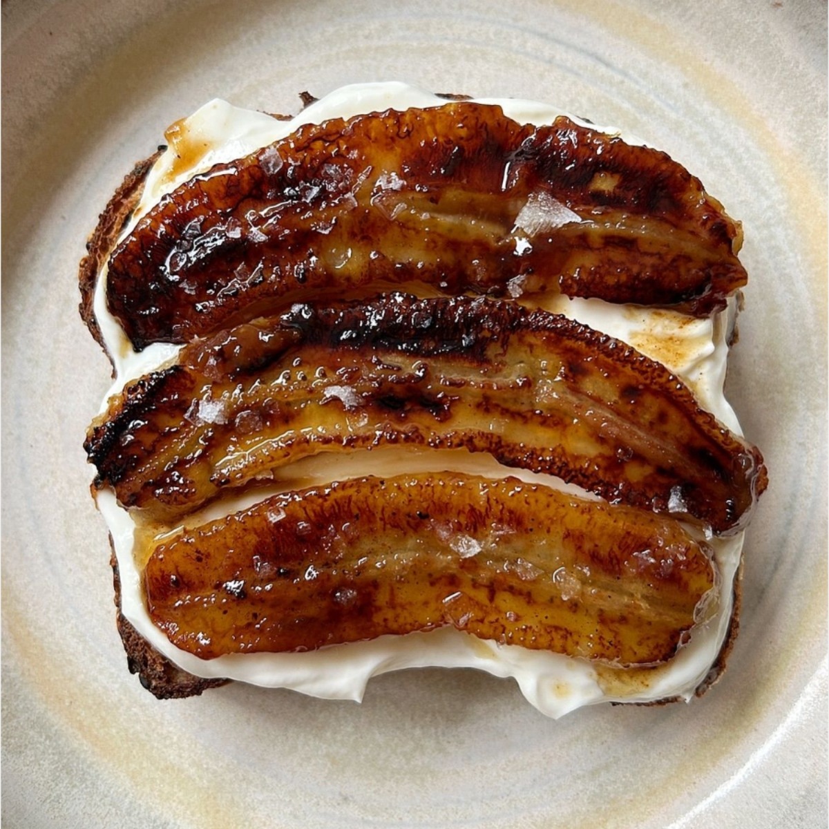 Caramelized banana halves on cream cheese toast on a beige ceramic plate