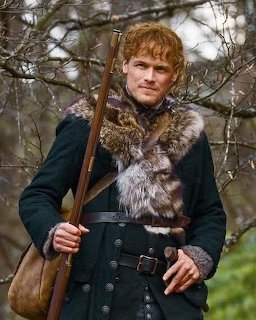 Red-haired man in green fur-collared coat holding a rifle in a forest