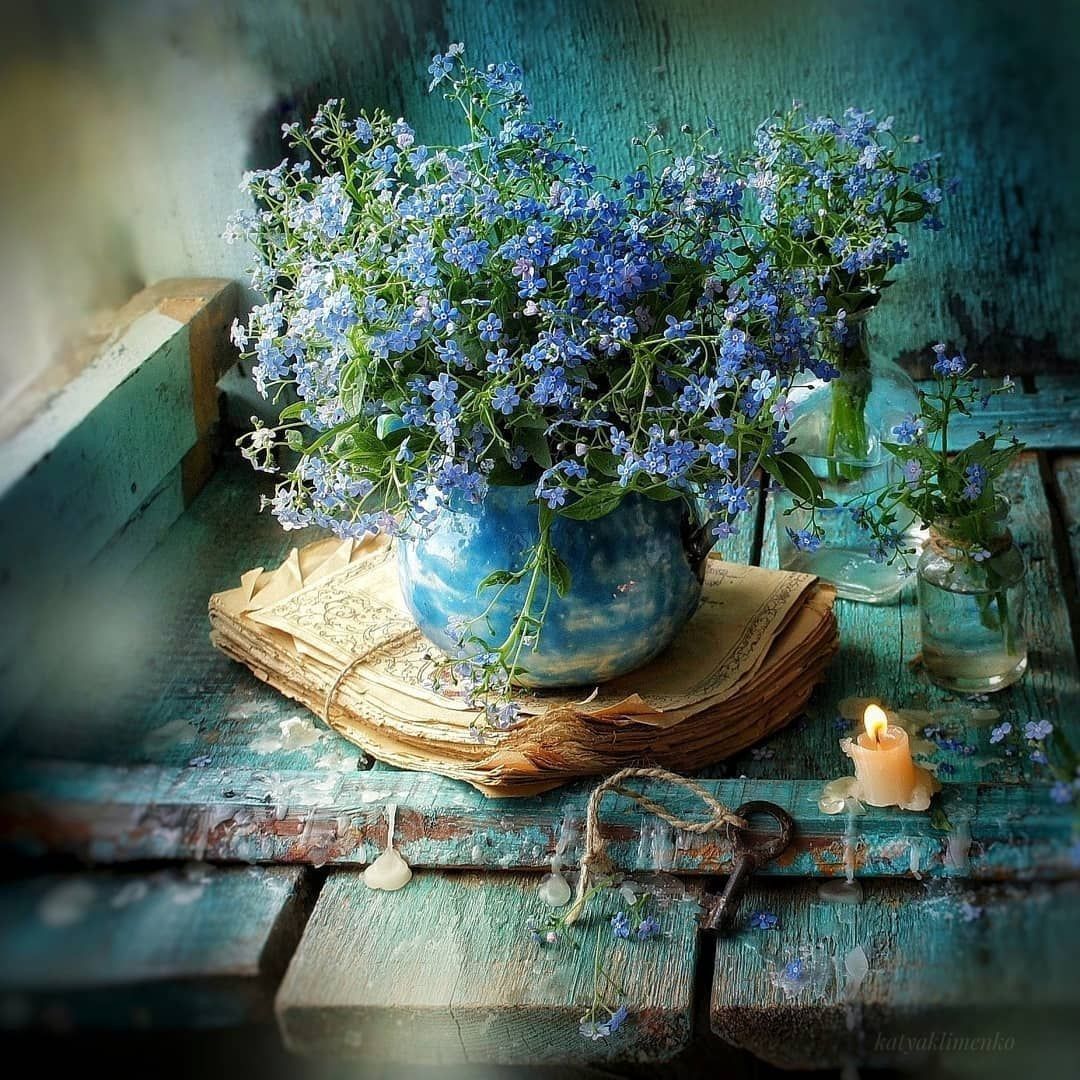 Blue forget-me-not flowers in vase on weathered wooden table with candle