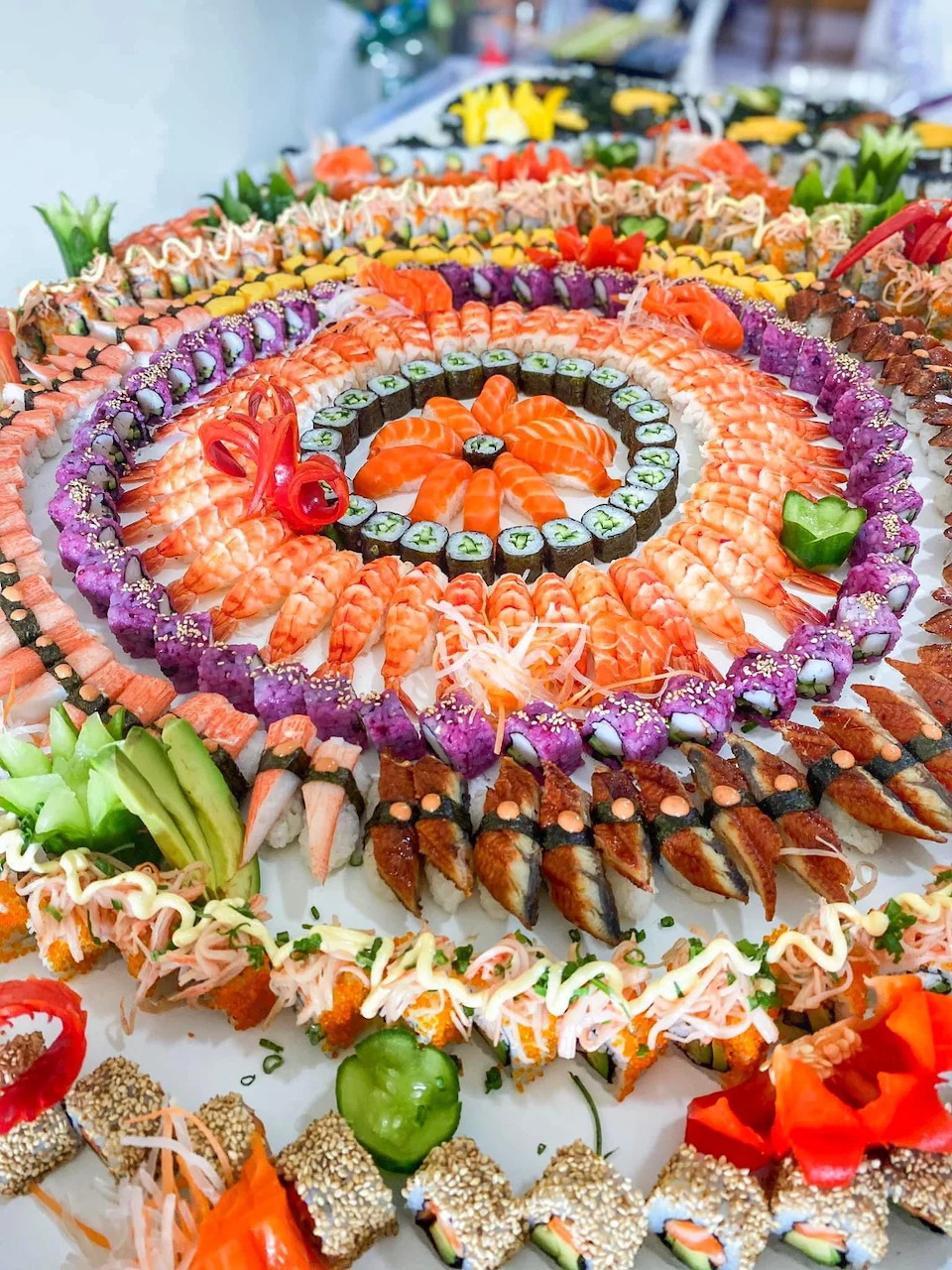 Large circular sushi platter with concentric rings of salmon, shrimp, maki rolls, and assorted seafood
