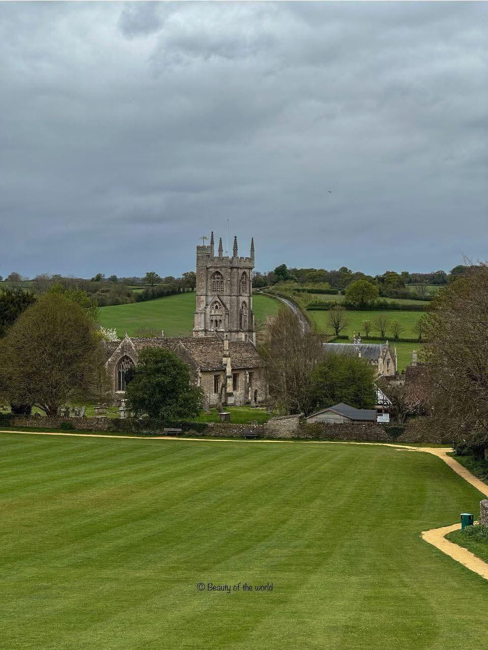 Stone church with tall tower in green countryside under overcast sky