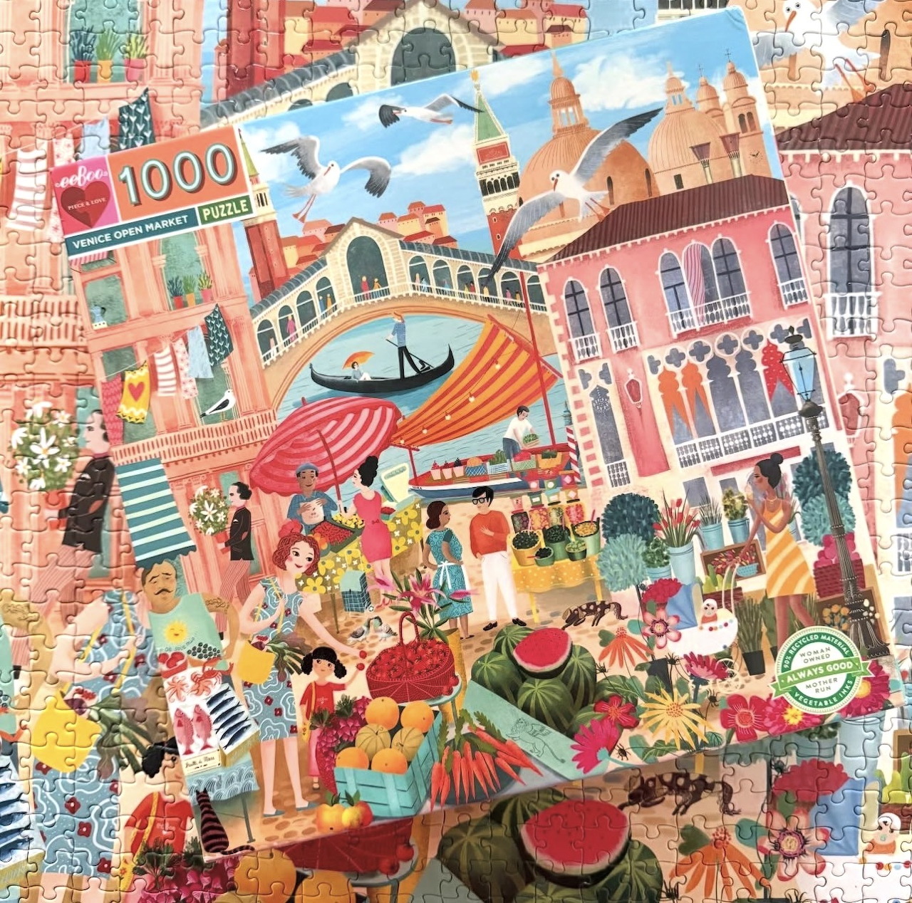 Colorful illustrated city market scene with fruit stalls, flowers, buildings, a gondola, and flying birds