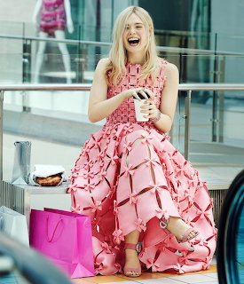 Woman in voluminous pink ruffled dress laughing while seated outdoors with shopping bags