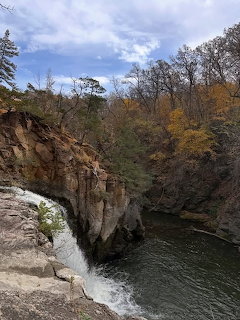 Rocky gorge with waterfall and autumn trees along river under a cloudy sky