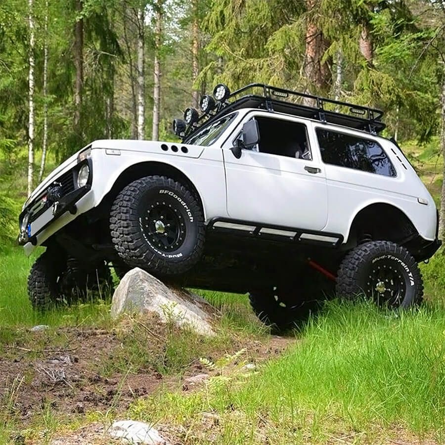 White lifted Lada Niva 4x4 driving over a rock in a grassy forest