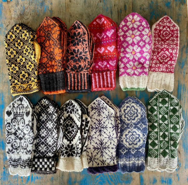 Twelve pairs of colorful patterned knit mittens displayed on weathered blue wood background