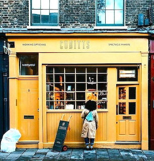 Person viewing yellow Cubitts glasses shop storefront with large grid windows