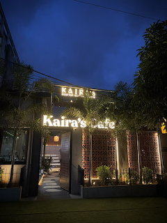 Illuminated Kaira's cafe storefront at twilight with glowing white sign and landscaped pathway